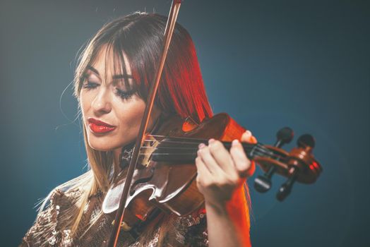 Beautiful young smiling woman in sequin dress playing the classical music on violin.