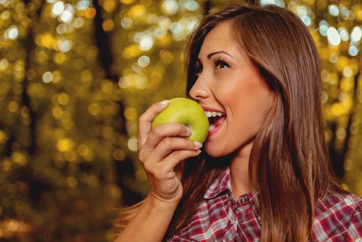 Beautiful smiling girl in the nature holding green apple and looking at camera.