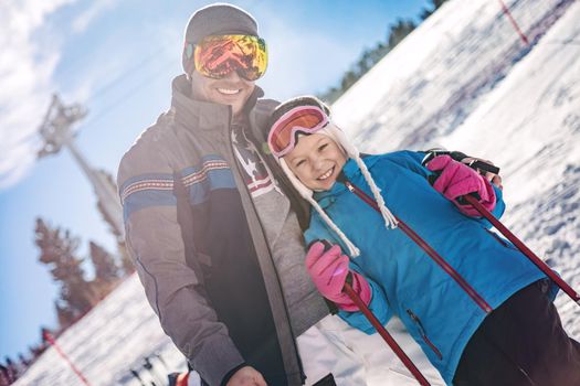 Beautiful young father and daughter enjoying in ski vacations. They are posing on sunny winter day and looking on camera with smile. 