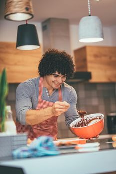 Young handsome man making cookies in his kitchen for his friends. He  is pouring chocolate dough into molds.