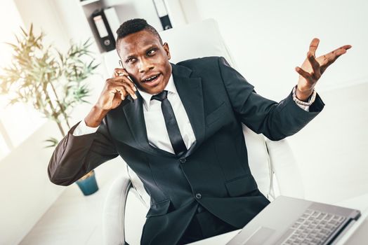 Pensive African businessman talking on smartphone in modern office. 