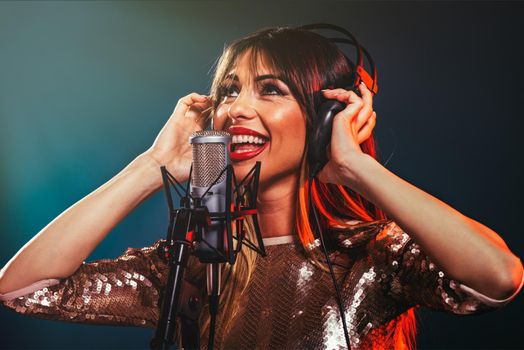 A young woman singer with headphones in front of the microphone. Sing with mouth wide open and with an expression of happiness on her face.