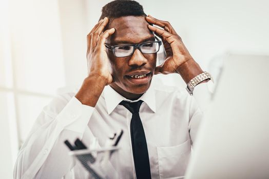 Anxious African businessman sits in the office and holds his head with his hands.