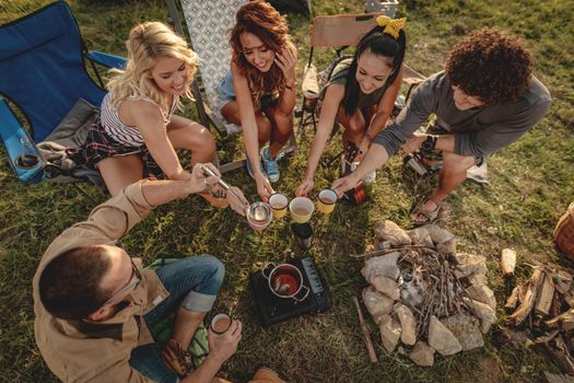 Happy young friends enjoy a sunny day in nature. They're cooking tea, laughing and talking happy to be together. Top view.