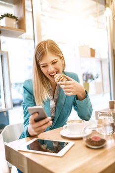 Young smiling businesswoman on a break in a cafe. He is having breakfast and using smartphone. 