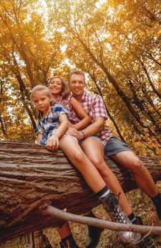 Beautiful young family sitting on fallen tree in the forest and enjoying.