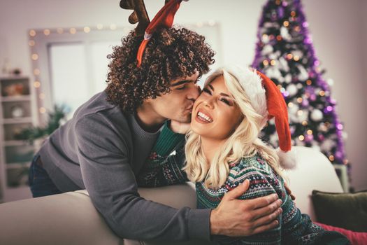 Loving couple in cozy warm sweaters on a Christmas - New Year eve, smiling, kissing, having fun with each other. 