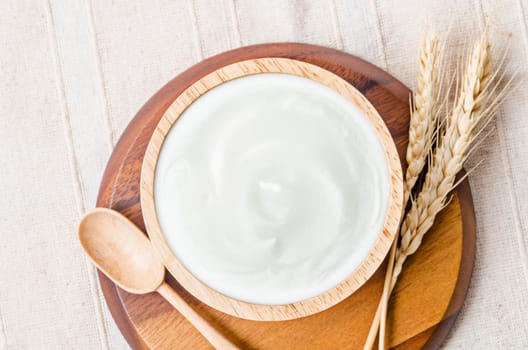 Greek yogurt in a wooden bowl and dry barley on tablecloth.