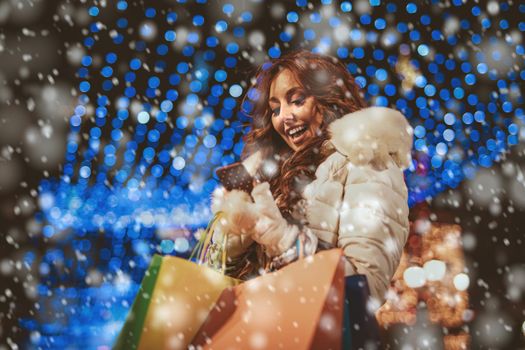 Cheerful young woman with colorful shopping bags using smartphone and having fun in the city street at Christmas time.
