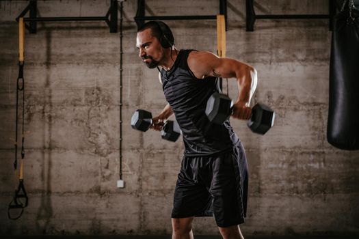 Young muscular man doing hard exercise with dumbbells for shoulders on cross fit training at the gym.