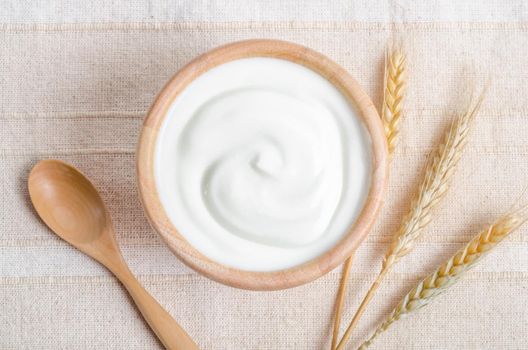 Greek yogurt in a wooden bowl and dry barley on tablecloth.
