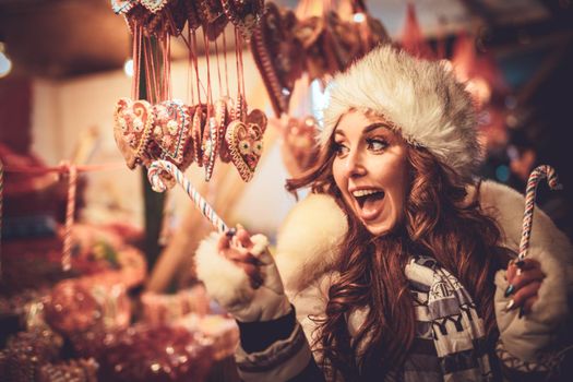 Cheerful young woman having fun on a Christmas market in the city street at the New Year night.