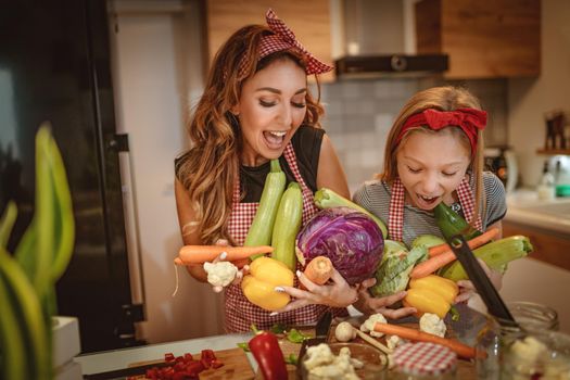 Happy mother and her daughter enjoy preparing for marinating vegetables and making healthy meal together with fun, at their home kitchen.  