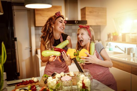 Happy mother and her daughter enjoy preparing for marinating vegetables and making healthy meal together at their home kitchen.  