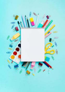 Online study, drawing, distantly painting class. Notebook, colorful stationery, supplies for drawing and craft. Empty notepad sketchbook sheet, shool supplies on blue. Vertical. Copy space, flatlay