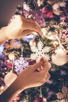 Beautiful smiling young woman decorating christmas tree with Christmas ornament at home.
