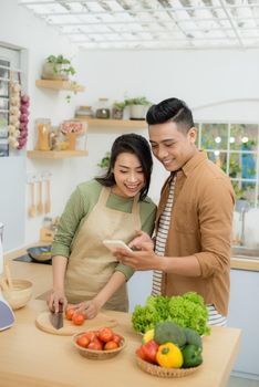 Beautiful young couple is using a cellphone and smiling while cooking in kitchen at home