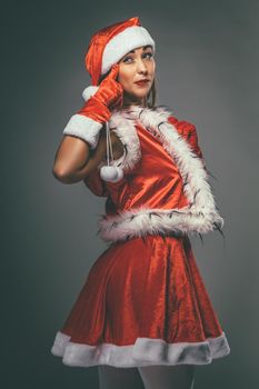 Beautiful young smiling woman in Santa Claus costume standing, looking at camera and thinking.