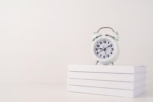 Time management, punctuality, business metaphors. Back to school. White alarm clock hands on nine ten on stack of books, mockup design, copy space