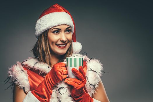 Portrait of a beautiful young smiling woman in Santa Claus costume. She is smiling and holding cup of hot tea.