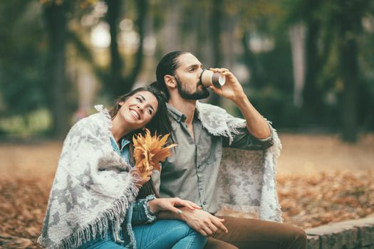 Beautiful smiling couple enjoying in sunny city park in autumn colors looking each other. They are having fun with yellow leaves.