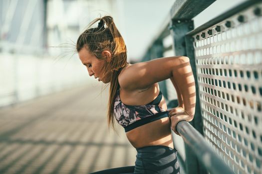 Young fitness woman doing hard exercise on river bridge, preparing for morning workout.