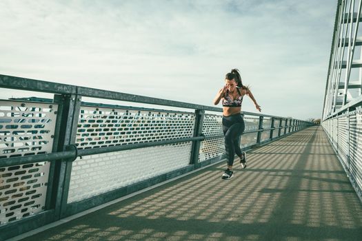 Fit muscular young woman runner sprinting at great speed outdoors on the river bridge.