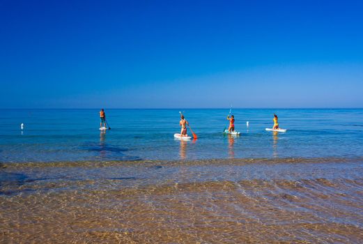 Stand up paddle boarding. Joyful group of friendsare training SUP board in the mediterranean sea on a sunny morning in Realmonte beach, Sicily. Italy