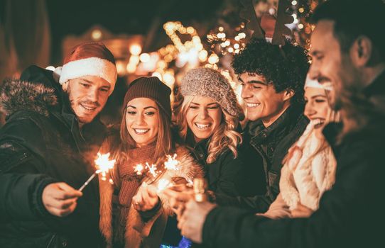 Three couple with sparklers enjoying Christmas outdoor party in the city street at night and with a lot of lights on background.