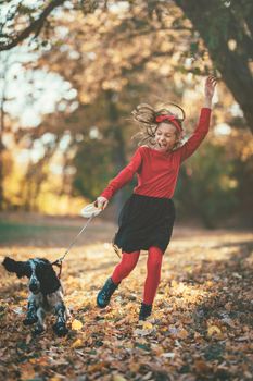 Beautiful happy little girl having fun in the forest with her pet dog in sunset. They are running and playing in happiness.