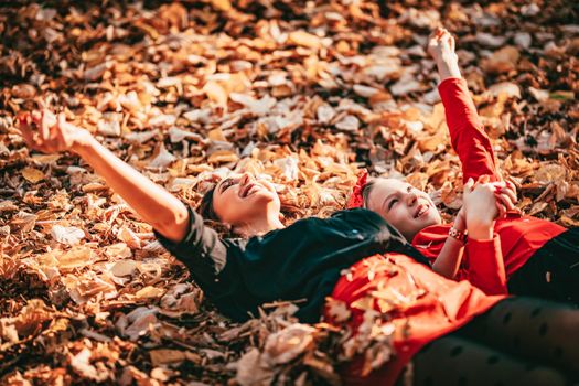 Beautiful young woman and her little daughter are enjoying in autumn sunny forest colors. They are lying down on golden yellow leaves and having fun. 
