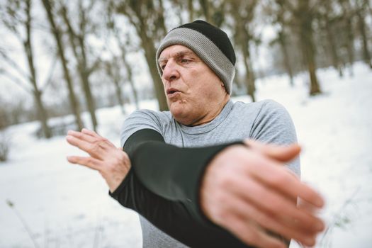 Active senior man stretching and doing exercises in public park during the winter training outside in.