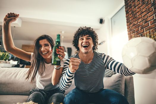 Couple are fans of sports games as football love spending their free time at home together. They are screaming and gesturing for a victory. 
