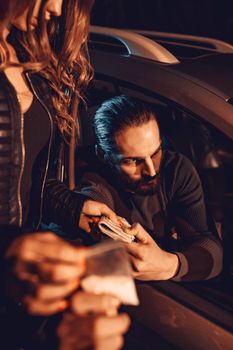 The dealer sells a little bag of heroin or cocaine to a young woman from a car, and she gives him money.