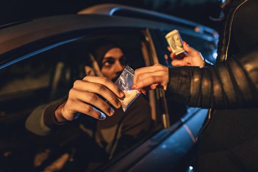 The dealer sells a little bag of heroin or cocaine to a young woman from a car, and she gives him money.