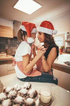 Happy mother and her daughter enjoy making cookies together at their home kitchen.
