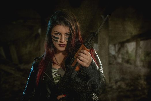 Attractive dark-haired girl in camouflage shirt hold machine gun leaning on the shoulder and with a dangerous expression on her face looking at the camera.