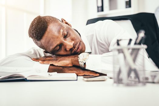 Tired African businessman is napping on desk next to documents late in the office.