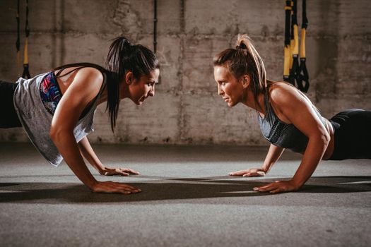 Two young muscular girls doing plank exercise at the cross fit workout.