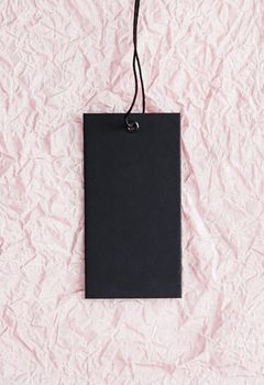 Black clothing tag on blush pink paper background, sustainable fashion and brand label concept.