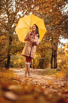 Happy woman with yellow umbrella walking in at beautifu sunny autumn park. 