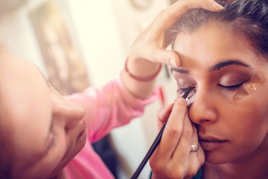 A portrait of a pretty woman having make-up applied by a makeup artist. Close-up.