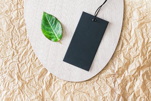 Clothing tag and green leaf as eco-friendly flatlay background, sustainable fashion and brand label concept.