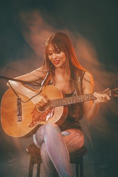 Beautiful young smiling woman sitting and playing the guitar with expression of happiness on her face.