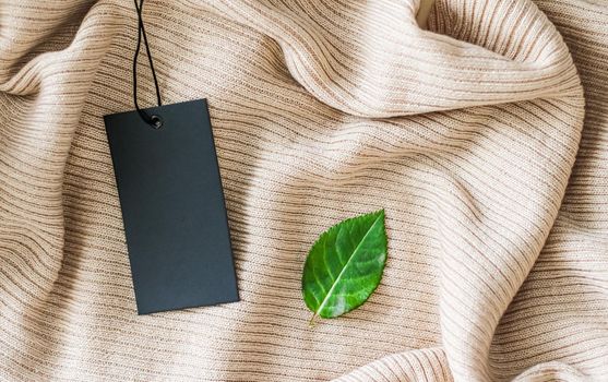 Clothing tag and green leaf as eco-friendly flatlay background, sustainable fashion and brand label concept.