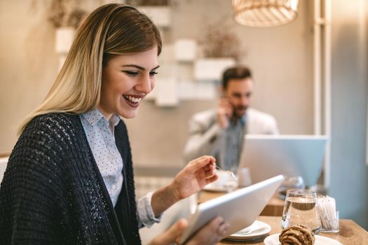 Young businesspeople surfing the internet on a break in a cafe. Smiling woman using digital tablet and drinking coffee. Man working at laptop and using smarthphone.