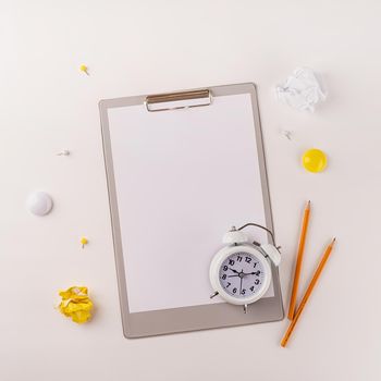 Business planning, time management concept. Blank paper on clipboard, white alarm clock and stationery top view on white table. Copy space, flat lay