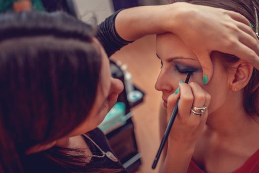 A portrait of a pretty woman having make-up applied by a makeup artist. Close-up.