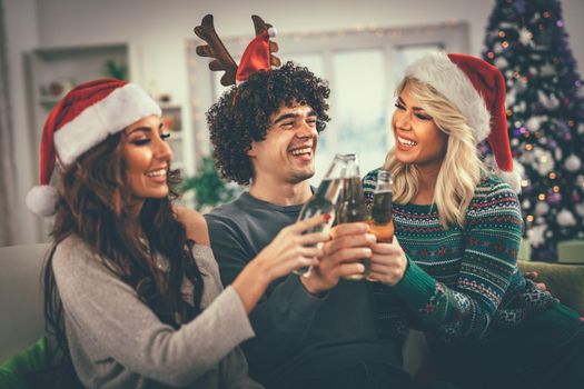 Group of friends celebrating Christmas at home, they are having fun and toasting with beer. Selective focus.