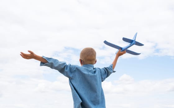 Rear view of a child boy with an airplane dreams of traveling in the summer in nature against the blue sky.